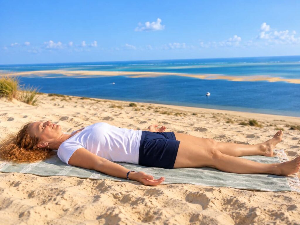 Femme allongée sur une serviette sur la plage, face au ciel.